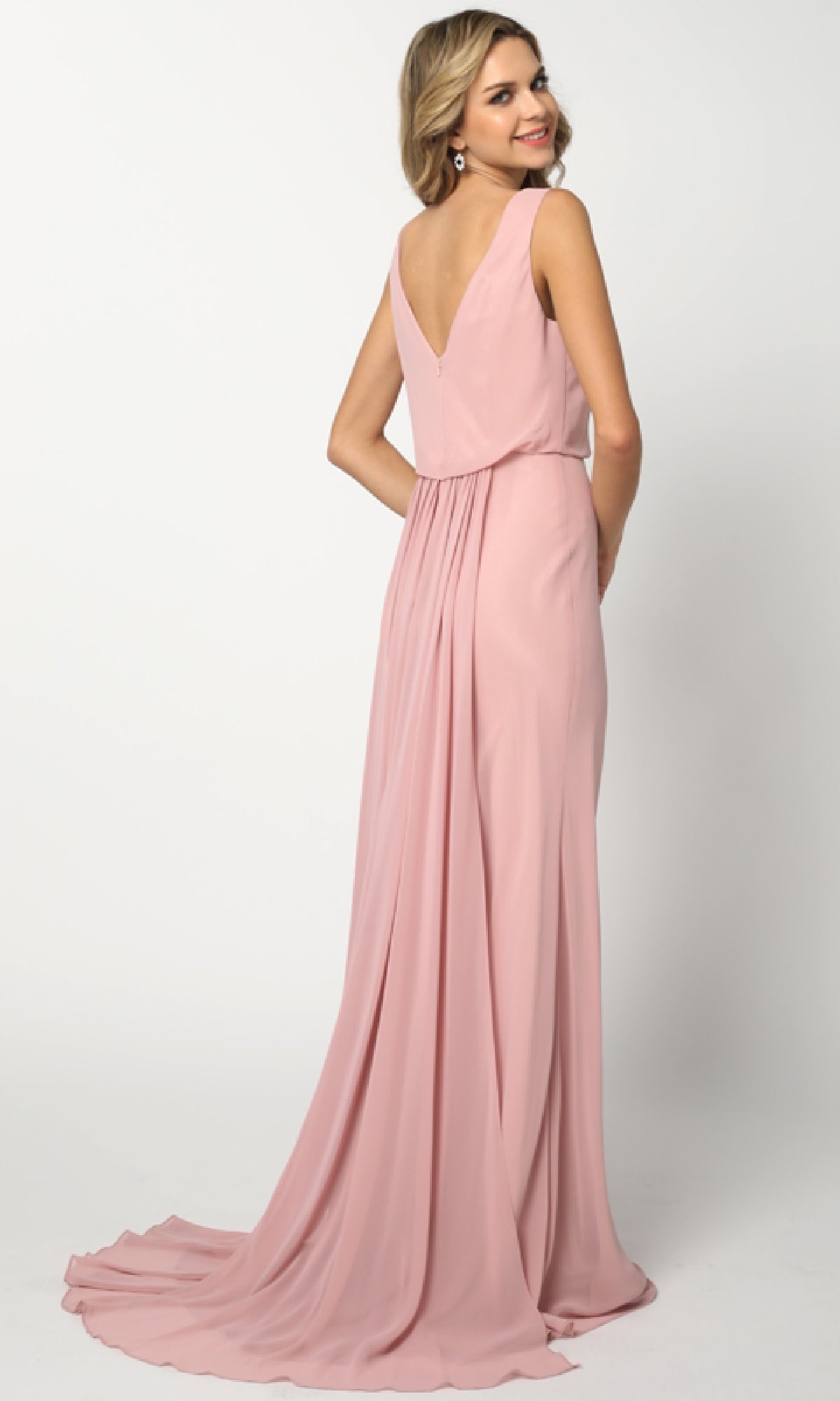A woman faces away in the Juliet 670 Long Prom Dress, featuring a sleeveless light pink design with a V-back, blouson bodice, and flowing train set against a plain white background.